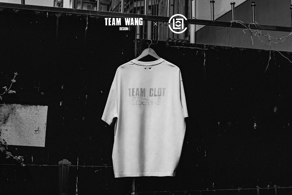 Black-and-white photo of a white TEAM CLOT T-shirt on a hanger against a dark wall, with TEAM WANG design and CLOT logos above